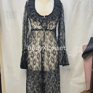 Può includere: Accappatoio in pizzo nero con maniche lunghe e scollatura a balze. L'accappatoio presenta un davanti allacciato e un design lungo e fluido. Il testo "BodyXCorse" è visibile sull'indumento.