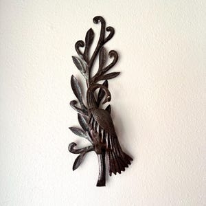 May include: A dark brown metal wall art piece depicting a bird perched on a branch with leaves. The bird has a long neck and detailed feathers. The leaves and branches have a textured appearance.