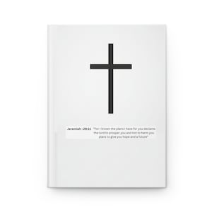 May include: White journal featuring a black cross design. The cover includes the text "Jeremiah 29:11" and a quote. This is a religious-themed notebook.