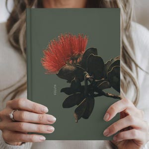 May include: A hardbound notebook with a matte olive green cover featuring a vibrant red pohutukawa flower and dark green leaves. The word NOTES is printed in small white capital letters on the left side of the cover, centered vertically.