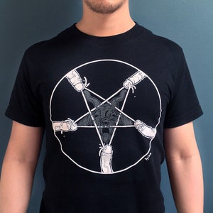 May include: A black short-sleeve t-shirt featuring a white circular graphic. Inside the circle is a pentagram formed by five phallic shapes pointing toward a central goat head illustration. The design includes thin white lines and a small signature.