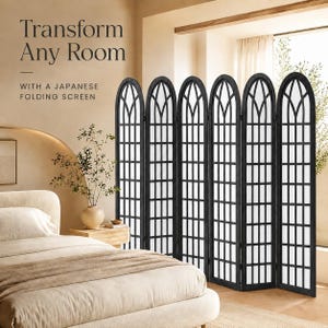 May include: A six-panel black folding screen featuring an arched top design with a grid pattern. The text on the image reads: Transform Any Room WITH A JAPANESE FOLDING SCREEN. The screen is positioned next to a bed with beige bedding and a vase.
