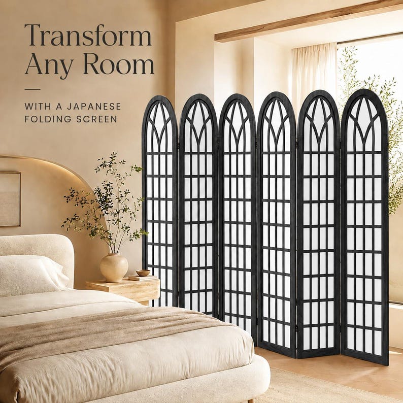 May include: A six-panel black folding screen featuring an arched top design with a grid pattern. The text on the image reads: Transform Any Room WITH A JAPANESE FOLDING SCREEN. The screen is positioned next to a bed with beige bedding and a vase.