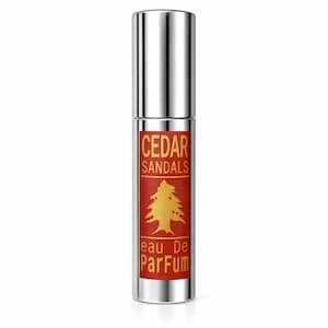 May include: A silver perfume bottle with a red label. The label has the text "CEDAR SANDALS" and a gold tree graphic. The words "eau De Parfum" are also on the label. The bottle has a shiny, metallic finish.