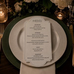 May include: A white die-cut menu card with black text centered on a white dinner plate. The menu lists a starter, entree, sides, and dessert, including items like house salad, garlic bread, pollo alla vesuvio, sausage, peppers, and wedding cake.