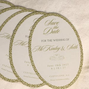 May include: Oval Save the Date cards with a gold lattice border. The text reads: Save the Date FOR THE WEDDING OF McKinley & Seth, June 18th 2027, 6 | 18 | 27, CLEVELAND, GA, Formal Invitation to Follow. Features a swan illustration.