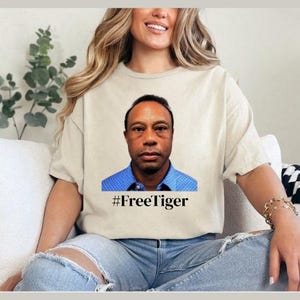 Puede incluir: Camiseta color crema con un retrato de un hombre con una camisa azul con cuello. El texto "#FreeTiger" está impreso debajo del retrato en negro. La camiseta la lleva una persona.
