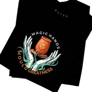 May include: Black t-shirt with a graphic design featuring a terracotta pot with a smiling sun face, held by stylized hands. The words "MAGIC HANDS" and "MOULD GREATNESS" are in a circle around the hands. The word "BLISS" is printed on the upper right.