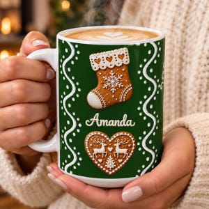 May include: A white ceramic mug with a dark green background featuring a white wavy dotted border. The mug displays a gingerbread stocking with white icing details, the name Amanda in white script, and a gingerbread heart with reindeer.
