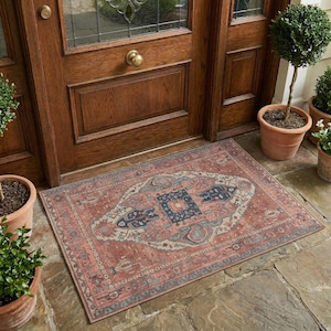 May include: A rectangular doormat featuring a detailed, intricate pattern in shades of terracotta, navy blue, and cream. The design includes a central medallion surrounded by ornate floral and geometric motifs, laid flat on a stone patio surface.