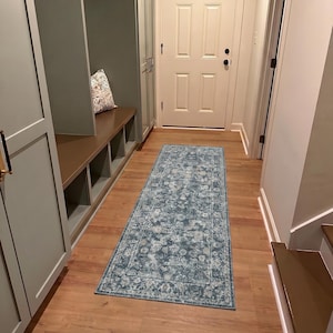 May include: A rectangular, distressed-look rug with a blue and white floral pattern. The rug is placed on a hardwood floor in a hallway, with a built-in bench and a white door visible in the background. The rug's dimensions are not visible.