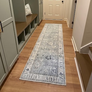 Könnte beinhalten: Ein langer, rechteckiger Läufer mit einem verblassten, abgenutzten Muster in den Farben Hellblau, Grau und Creme. Der Teppich zeigt ein zentrales Medaillon-Design, das von einer dekorativen Bordüre mit komplexen, geometrischen Motiven umgeben ist.