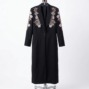 Puede incluir: Abrigo largo negro con bordados florales en rosa, verde y rojo. Los bordados están en las solapas y mangas. El abrigo tiene un cierre de un solo botón y un diseño clásico.