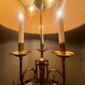 May include: A vintage brass candelabra-style lamp with three candle-shaped bulbs and a large lampshade. The lamp has a gold finish and a decorative design, with a warm, inviting glow.