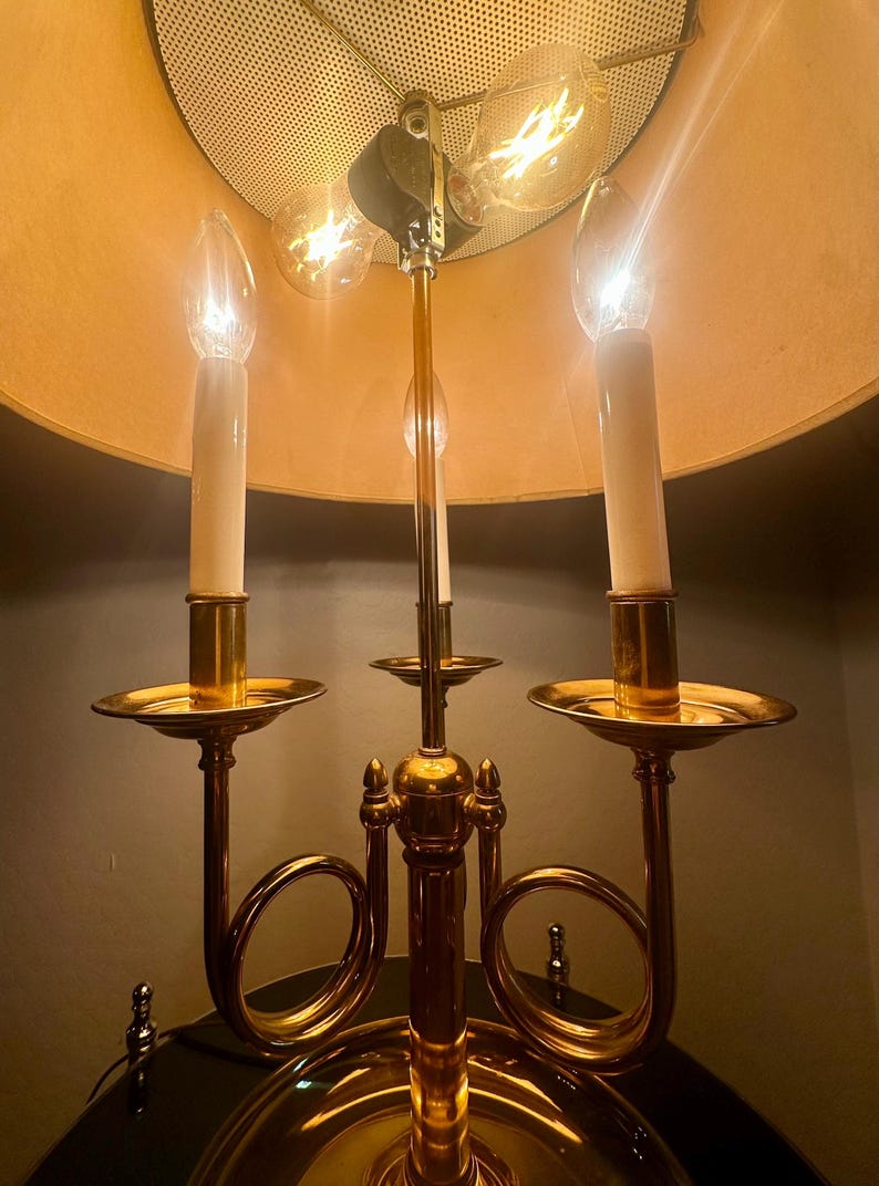 May include: A vintage brass candelabra-style lamp with three candle-shaped bulbs and a large lampshade. The lamp has a gold finish and a decorative design, with a warm, inviting glow.