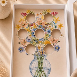 May include: A white box with a floral design featuring a watercolor painting of a bouquet of flowers in a blue vase. The box has eight circular cutouts. The flowers are in shades of yellow, pink, blue, and white.