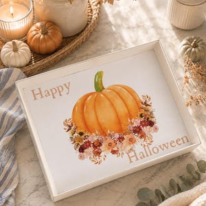 May include: A rectangular white tray featuring a central watercolor illustration of a bright orange pumpkin with a green stem, surrounded by a cluster of autumn-colored flowers and leaves. The text Happy Halloween is printed in a light brown font.