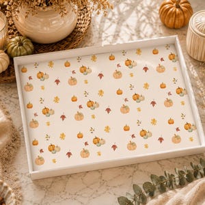 May include: A rectangular white serving tray featuring a repeating pattern of small orange pumpkins and autumn leaves in shades of red, yellow, and brown scattered across a cream-colored background. The tray has a smooth, flat surface.