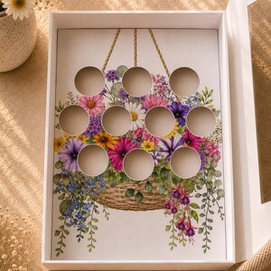 May include: A white box with a floral design featuring a basket overflowing with colorful flowers. The box has 12 circular cutouts. The flowers include pink, purple, yellow, and blue blooms. The box is open, revealing the interior.