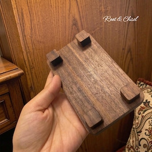 May include: A rectangular dark brown wooden display stand featuring four small square feet on the underside. The surface of the wood shows a natural grain pattern. The text Root & Chisel is visible in the upper right corner of the image.