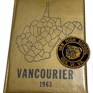 May include: A gold-colored yearbook titled "Vancourier 1963" with a map of West Virginia and a school patch. The patch is circular, navy blue with gold lettering and a bulldog graphic. The yearbook cover has a textured finish.