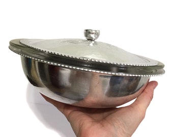 May include: A silver serving bowl with a glass lid. The bowl has a hammered finish and a beaded edge. The lid has a small knob on top.