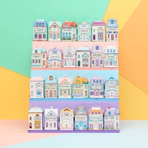 Puede incluir: Una colección de pequeños tarros de especias de cerámica con forma de casas coloridas. Cada casa presenta un nombre de especia diferente, como "Ajo", "Laurel" y "Azafrán". Los tarros están dispuestos en estantes escalonados sobre un fondo vibrante.