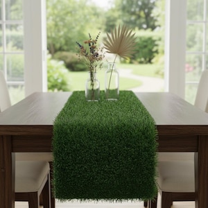 May include: A dark wooden dining table with a vibrant green grass runner. Two clear glass vases hold dried flowers and a large palm leaf. The table is set in front of a window overlooking a green yard.