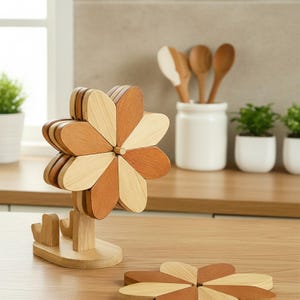 Könnte beinhalten: Ein hölzerner, blumenförmiger Untersetzer mit abwechselnd hellen und dunklen Holzblättern. Der Untersetzer steht auf einem Holzständer. Ein zweiter Untersetzer ist auf der Holzoberfläche sichtbar. Küchendekoration.
