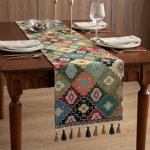 May include: A patterned table runner in a geometric design, featuring green, orange, red, and blue hues. The runner, adorned with tassels, rests on a wooden table set with plates, cutlery, and glasses. The table runner measures approximately 180 cm in length.