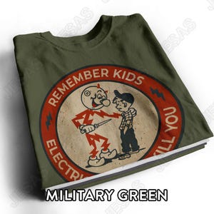 Puede incluir: Una camiseta verde militar con un gráfico circular de estilo dibujo animado vintage. El diseño muestra a un personaje con forma de rayo sosteniendo un cuchillo junto a un niño, con el texto "REMEMBER KIDS ELECTRICITY WILL KILL YOU".