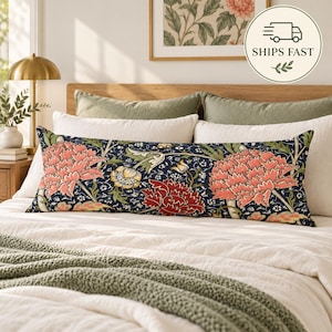 Pode incluir: Uma almofada lombar retangular longa com um fundo azul-marinho escuro e um padrão botânico denso de grandes cravos rosa-coral, flores vermelho-profundo e folhagem verde suave. A almofada está centrada sobre uma cama branca.
