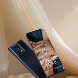 May include: Two black smartphones, one displaying the text "ENDLESS LOVE HAPPY MOTHER'S DAY" over an image of hands. The other phone shows the back with the camera lenses. The background features draped fabric.