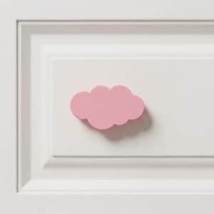 May include: A solid, matte, light pink cloud-shaped knob or handle mounted on a white, rectangular, paneled surface. The cloud shape features rounded, scalloped edges and a smooth, uniform finish, casting a soft shadow on the white panel.