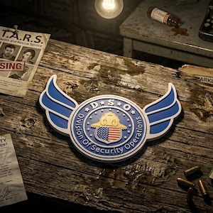 Pode incluir: Um emblema azul e branco da Division of Security Operations com asas e um escudo central com a bandeira americana, rodeado por um cartaz de pessoas desaparecidas, uma carta da polícia de Raccoon City e uma caixa de fita de máquina.