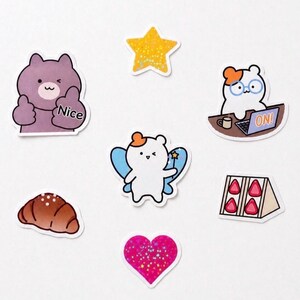 May include: A collection of colorful stickers featuring cute cartoon characters and objects. Includes a purple bear with a thumbs-up and the word "Nice", a yellow glitter star, a bear with glasses working on a laptop with "ON!" on the screen, a croissant, a fairy bear, a heart, and a strawberry sandwich.