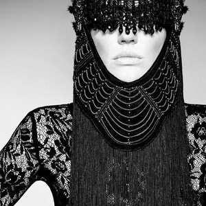 May include: A black and white photo of a person wearing a black lace outfit with a beaded headpiece that covers their eyes.