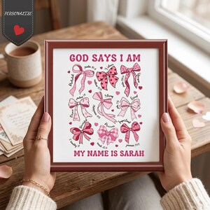 Peut inclure: Impression encadrée avec une bordure marron, avec le texte "GOD SAYS I AM" et "MY NAME IS SARAH". L'œuvre d'art comprend des nœuds roses avec des mots comme "Protégé", "Aimé" et "Unique". Le fond est blanc.