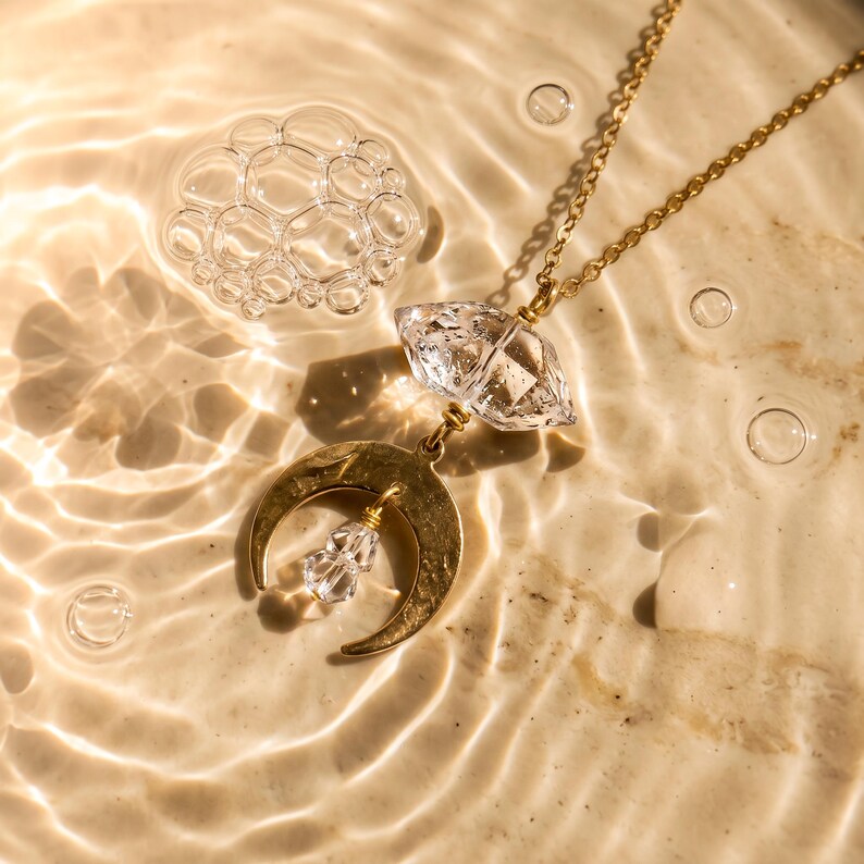 Pu&ograve; includere: Una collana color oro con una catenina sottile, un ciondolo in cristallo trasparente sfaccettato e un ciondolo a forma di mezzaluna dorata. Una piccola perla di cristallo trasparente pende dal centro della mezzaluna, unita da fili dorati.