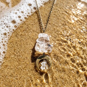 Pu&ograve; includere: Una collana con catena color bronzo, un grande cristallo di quarzo trasparente grezzo e un ciondolo a mezzaluna. Un cristallo trasparente pi&ugrave; piccolo e sfaccettato pende dal centro della mezzaluna, creando un design a strati.