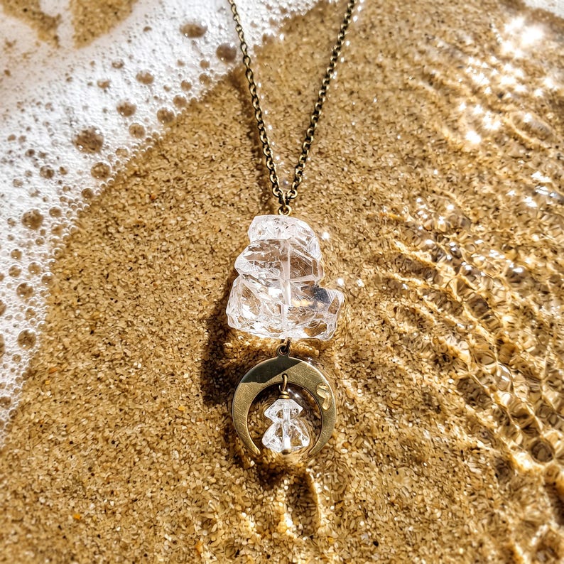 Pu&ograve; includere: Una collana con catena color bronzo, un grande cristallo di quarzo trasparente grezzo e un ciondolo a mezzaluna. Un cristallo trasparente pi&ugrave; piccolo e sfaccettato pende dal centro della mezzaluna, creando un design a strati.