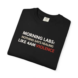 Könnte beinhalten: Schwarzes T-Shirt mit weißem und rotem Text. Der Text lautet: "MORNING LABS: NOTHING SAYS HEALING LIKE 4AM VIOLENCE". Das T-Shirt ist gefaltet und hat ein Etikett am Kragen.
