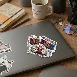 Könnte beinhalten: Ein Aufkleber auf einem Laptop zeigt einen gestressten Cartoon-Onigiri-Charakter. Der Text lautet "99% Stress, 1% Reis". Der Aufkleber ist weiß mit roten, blauen und schwarzen Akzenten. Eine Kaffeetasse und ein Notizbuch sind im Hintergrund.