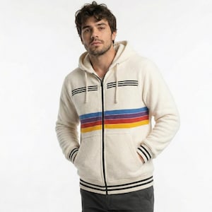 Puede incluir: Sudadera con capucha con cremallera de color crema con un diseño de rayas arcoíris en el pecho. La sudadera con capucha presenta rayas negras en la parte superior del pecho, los puños y el dobladillo inferior. Tiene capucha y dos bolsillos delanteros.