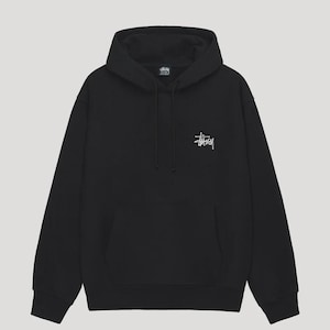 Pode incluir: Uma camisola preta de manga comprida com capuz, cordão ajustável e um bolso frontal tipo canguru. A peça apresenta um pequeno logótipo Stüssy branco estampado no lado esquerdo do peito. O design inclui punhos e bainha canelados.