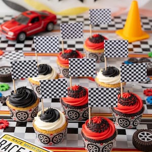 Può includere: Una scena di festa a tema auto da corsa con cupcakes ricoperti di glassa nera, bianca e rossa e bandiere a scacchi. Sono presenti anche un'auto giocattolo rossa, un cono arancione e un cartello con la scritta "Race Day". I cupcakes sono in involucri con un design di pneumatici.