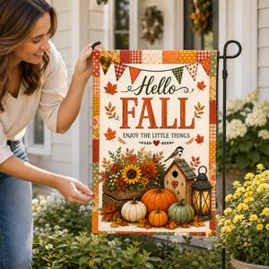 Puede incluir: Una bandera de jardín rectangular con un borde de patchwork y el texto Hello FALL ENJOY THE LITTLE THINGS. El diseño incluye hojas de otoño, una caja de madera con girasoles, calabazas, una casa para pájaros con un ave y un farol negro.