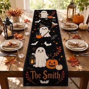 May include: A black rectangular table runner featuring a Halloween pattern with white ghosts, orange pumpkins, bats, and stars. The design includes the text The Smith in orange lettering at the bottom, surrounded by decorative autumn foliage and vines.