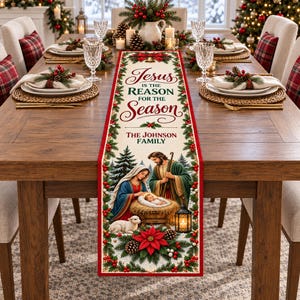 May include: A rectangular fabric table runner featuring a nativity scene with Mary, Joseph, and baby Jesus in a manger. The design includes red poinsettias, pine branches, and the text "Jesus IS THE REASON FOR THE Season" and "THE JOHNSON FAMILY".