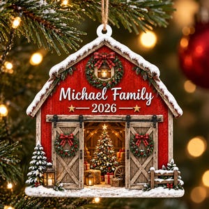 May include: A red barn-shaped Christmas ornament featuring a snow-covered roof, a wreath with a plaid bow, and sliding doors. The text reads Michael Family 2026. The interior shows a decorated Christmas tree, gifts, and lanterns, all hanging from a string.